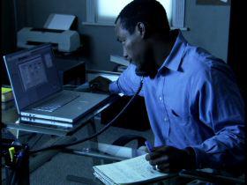 medium shot of a man as he chats on the phone and writes a note while working late in his home office
