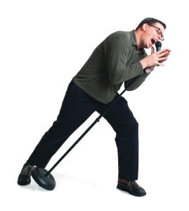 a caucasian man dressed in black pants and a green sweater dances and sings at a microphone