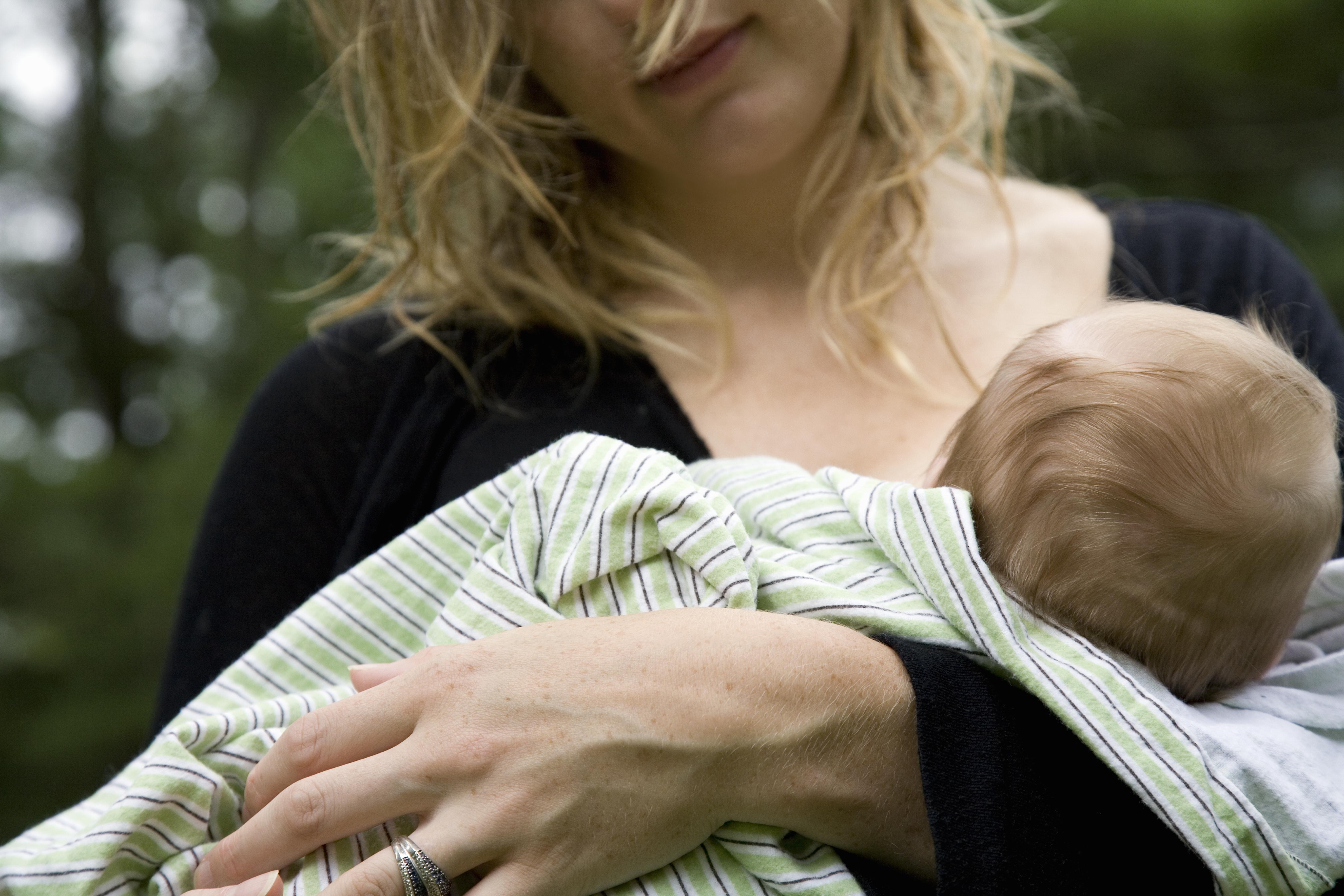 Mother breastfeeding baby girl (2-4 months) outdoors, mid section