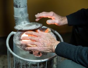 Elderly man warming up in a stove of fuelwood