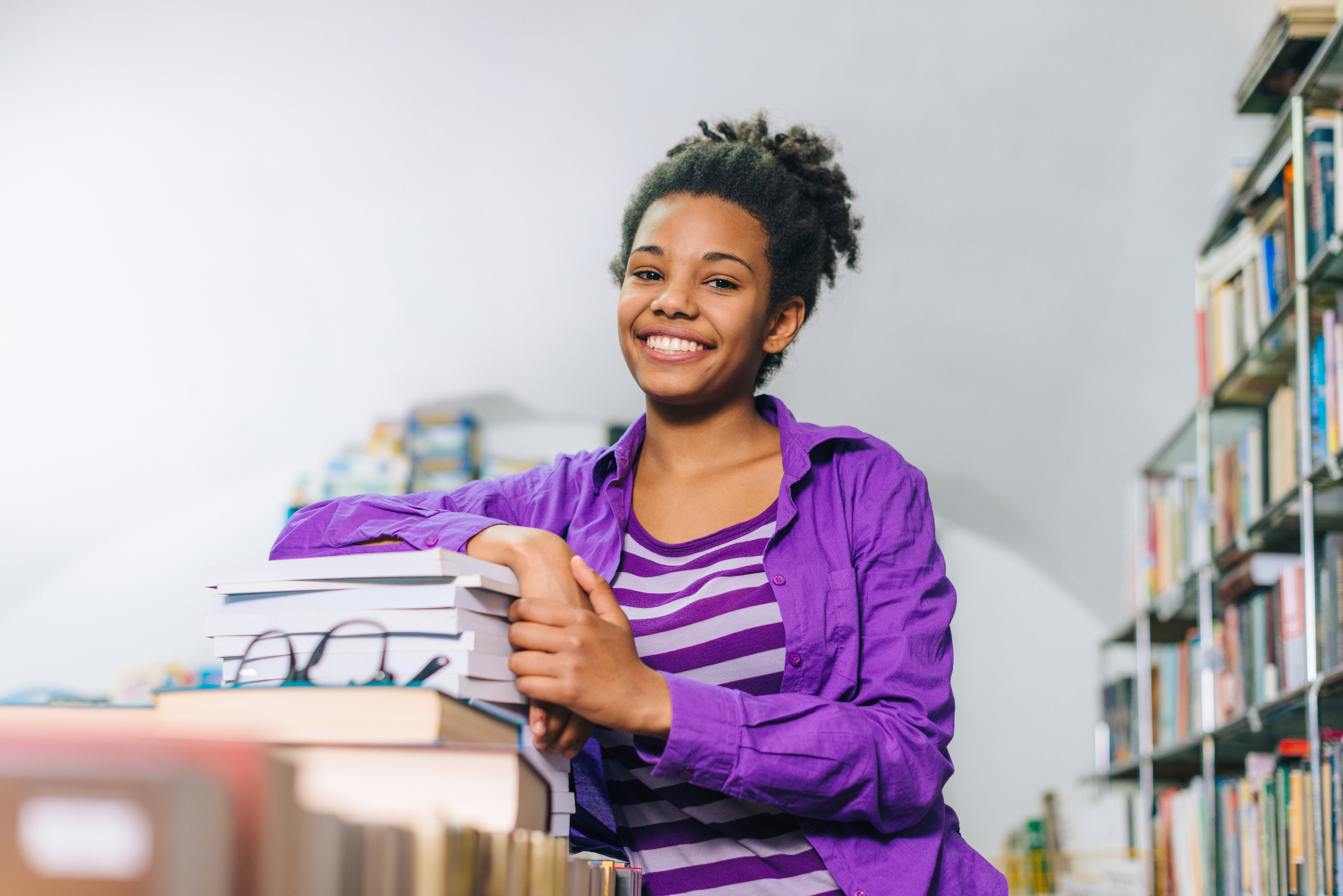 Pensive black girl in library posing with books