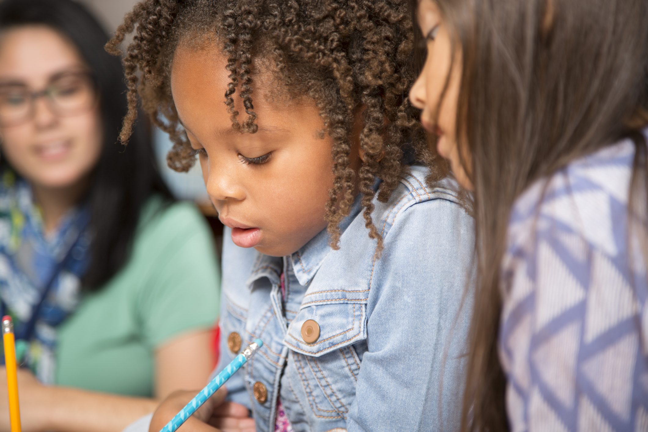 Teacher, mentor helps elementary-age schoolgirls with homework.