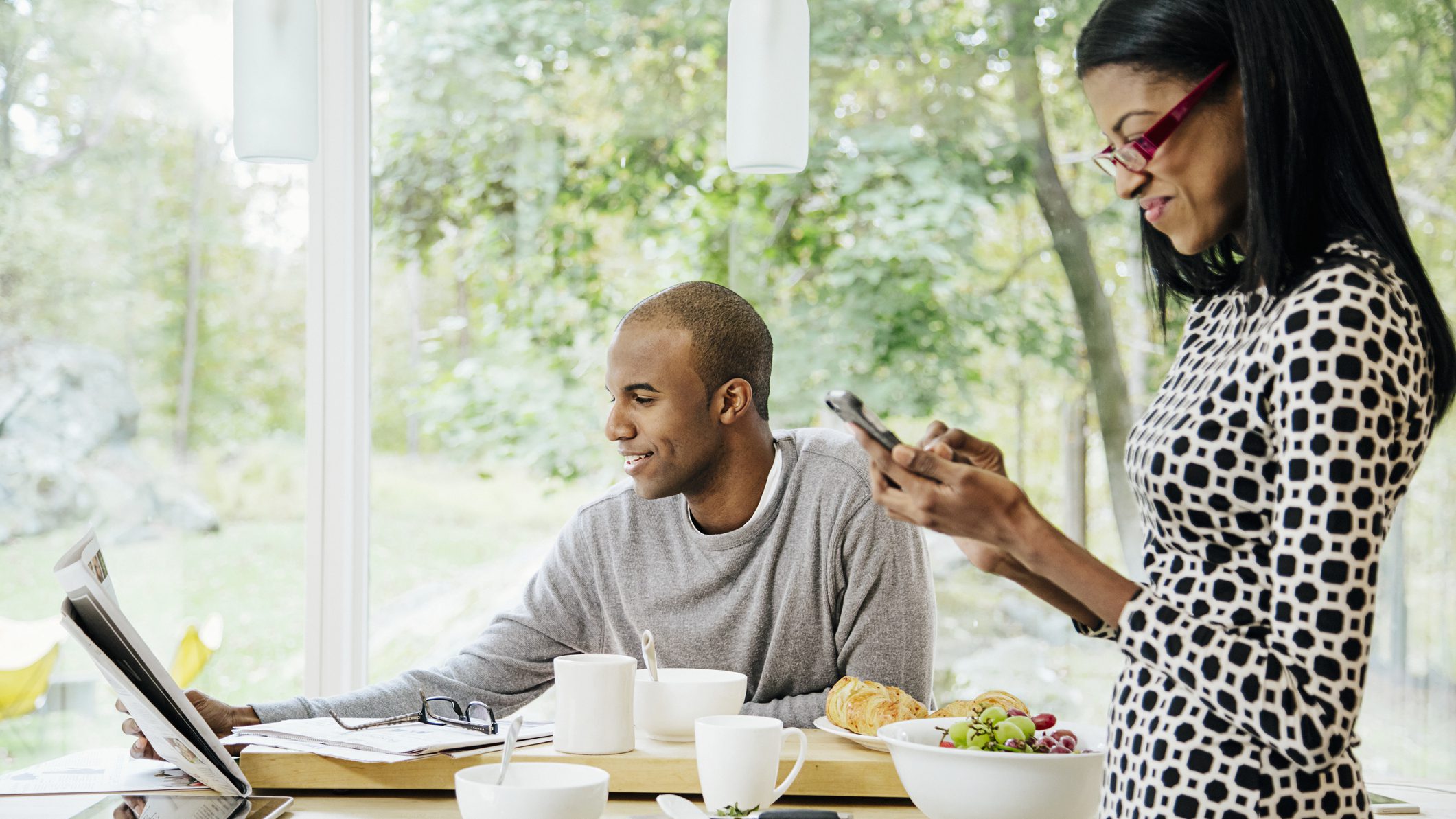 Mid-adult heterosexual couple eating breakfast, Reading newspaper and text messaging