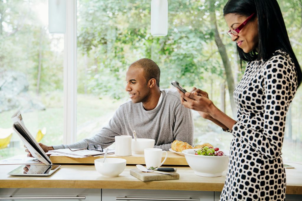 Mid-adult heterosexual couple eating breakfast, Reading newspaper and text messaging