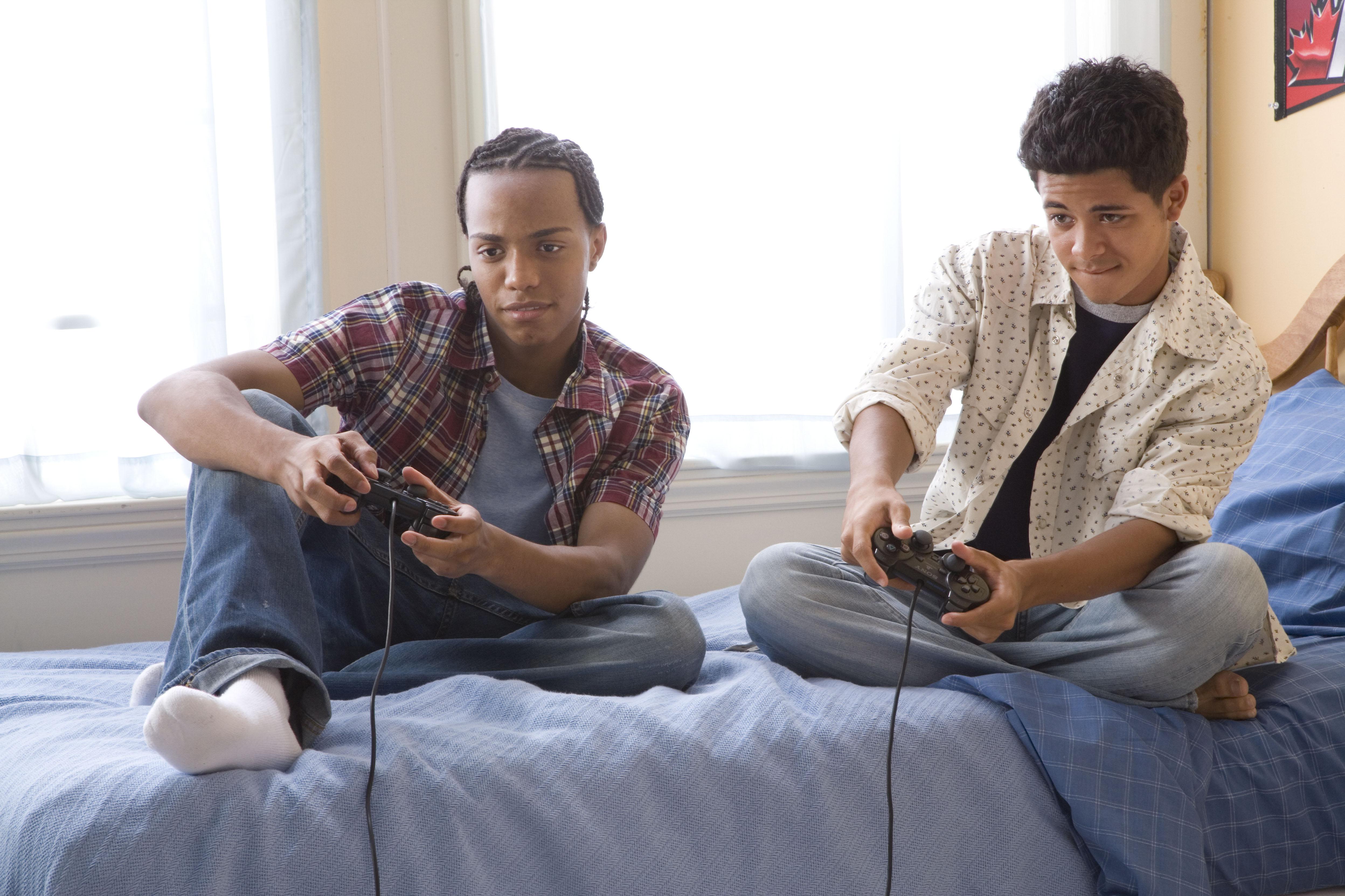 Two teenage boys (16-17) playing video games on bed