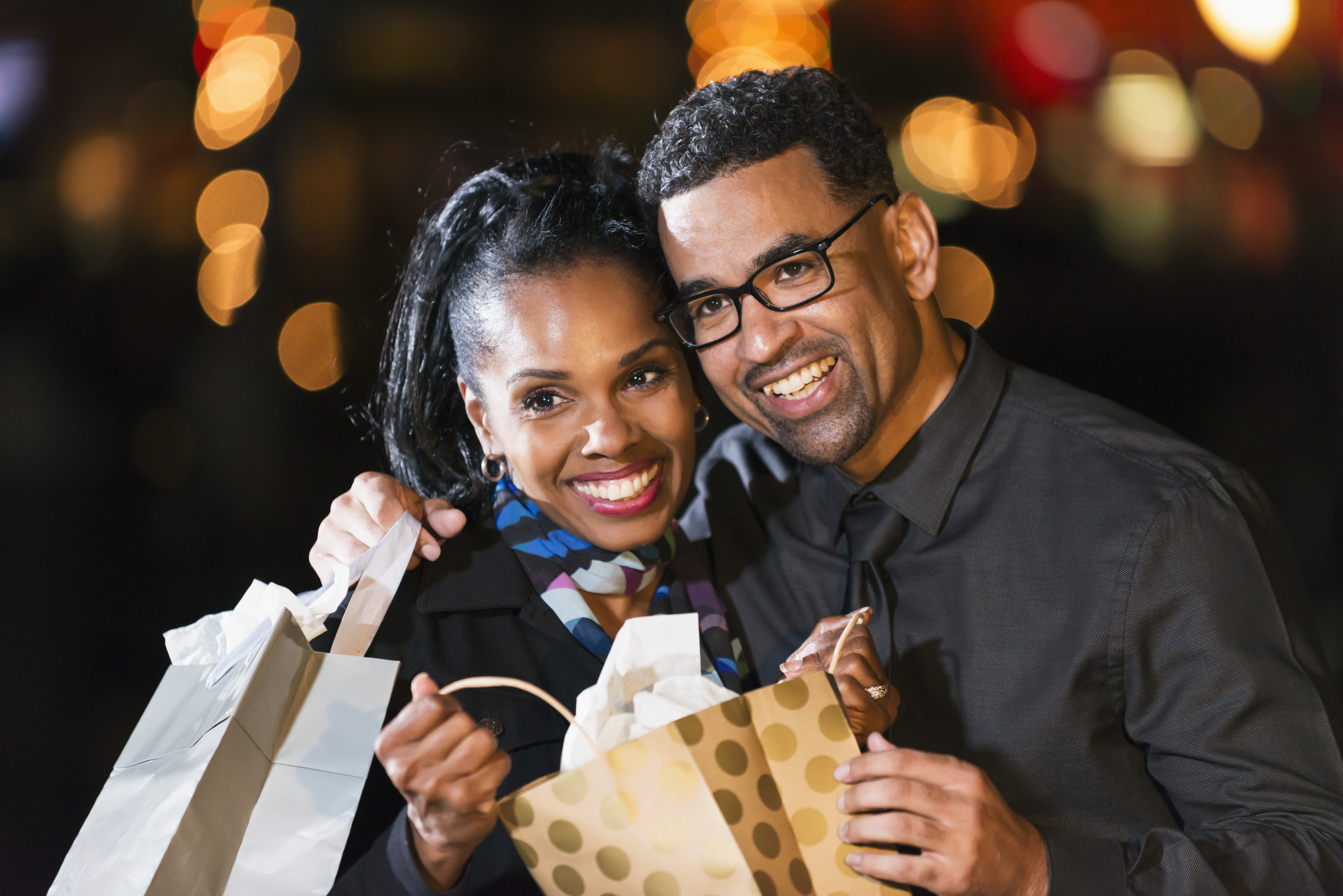 Happy black couple opening a gift bag outdoors at night