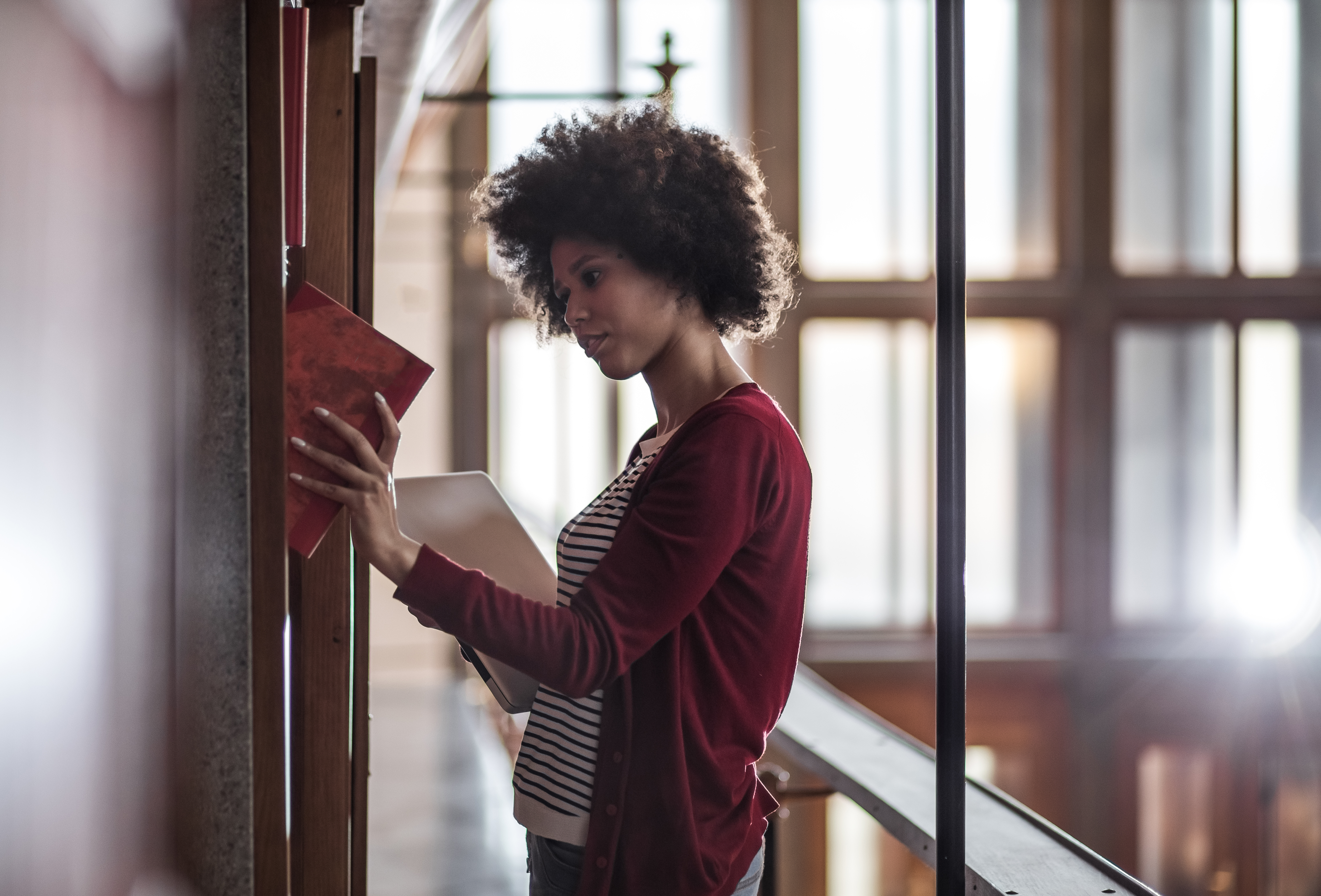 Young Woman in the Library Standing Beside The BookShelf and Studying