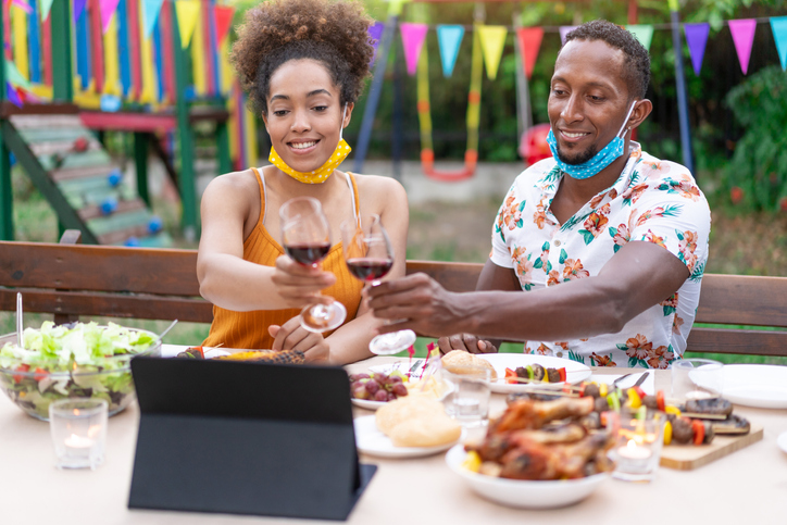 Afro Couple wearing protective face mask having staycation romantic dinner on back yard and making teleconferencing, during COVID-19.