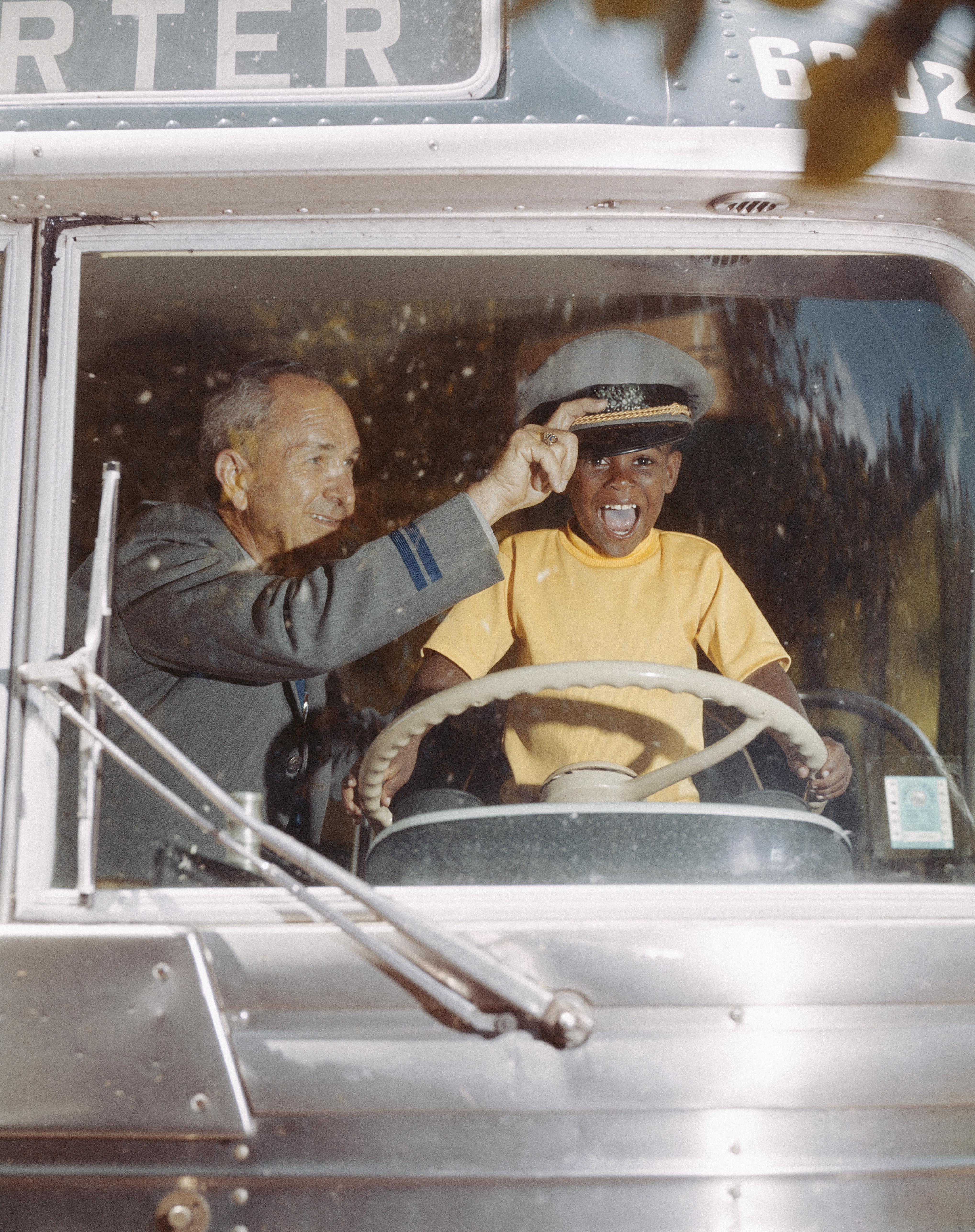 Bus driver giving hat to happy boy holding steering wheel