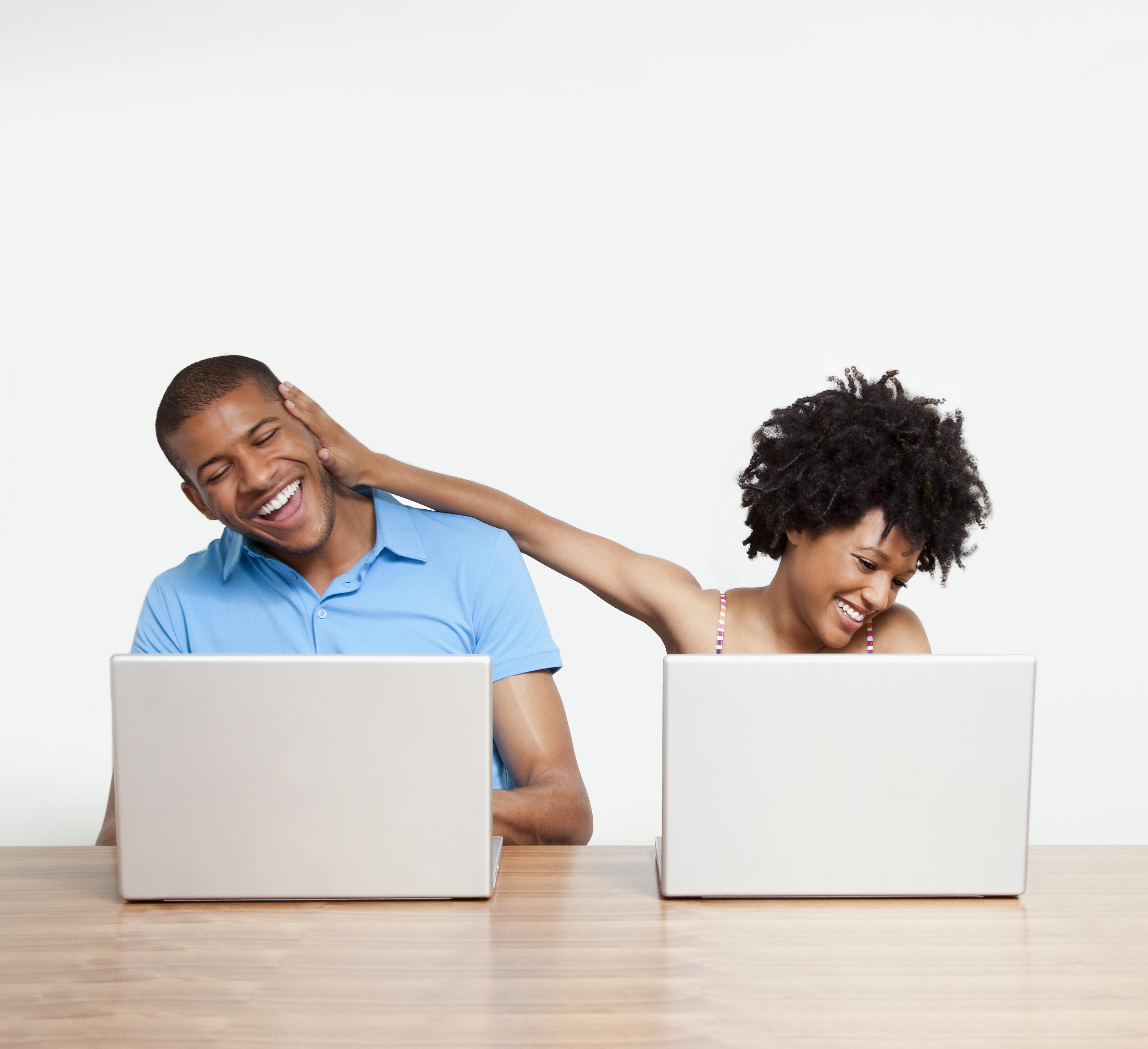 Woman joking with man as they work on laptops