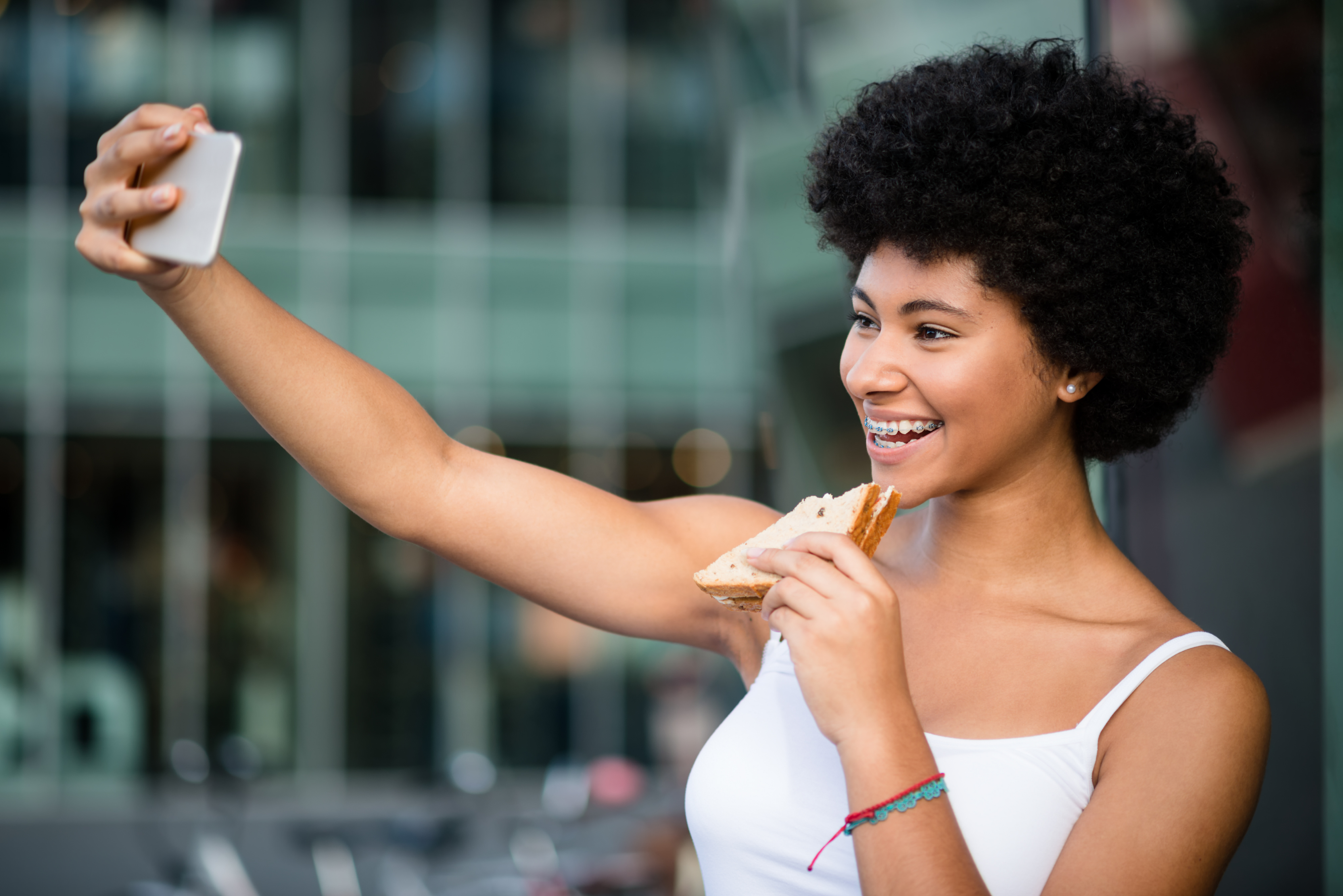 Young girl having fun outdoors. Taking selfie while eating sandwich.
