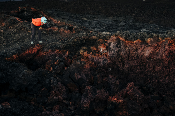 A woman looks into a deep hole that formed in a volcanic lava flow in Hawaii