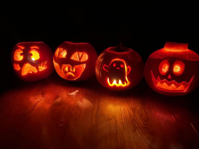 Closeup shot of four carved pumpkins, on a wooden floor, illuminated in the darkness