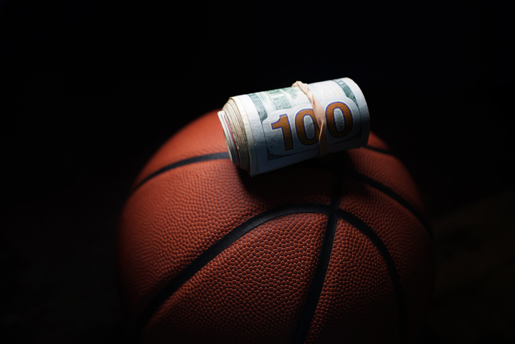 Rolled hundred dollar bill on a basketball, on black background
